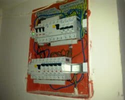 Czerwony panel elektryczny montowany na ścianie z przewodami, zainstalowany przez elektryka.